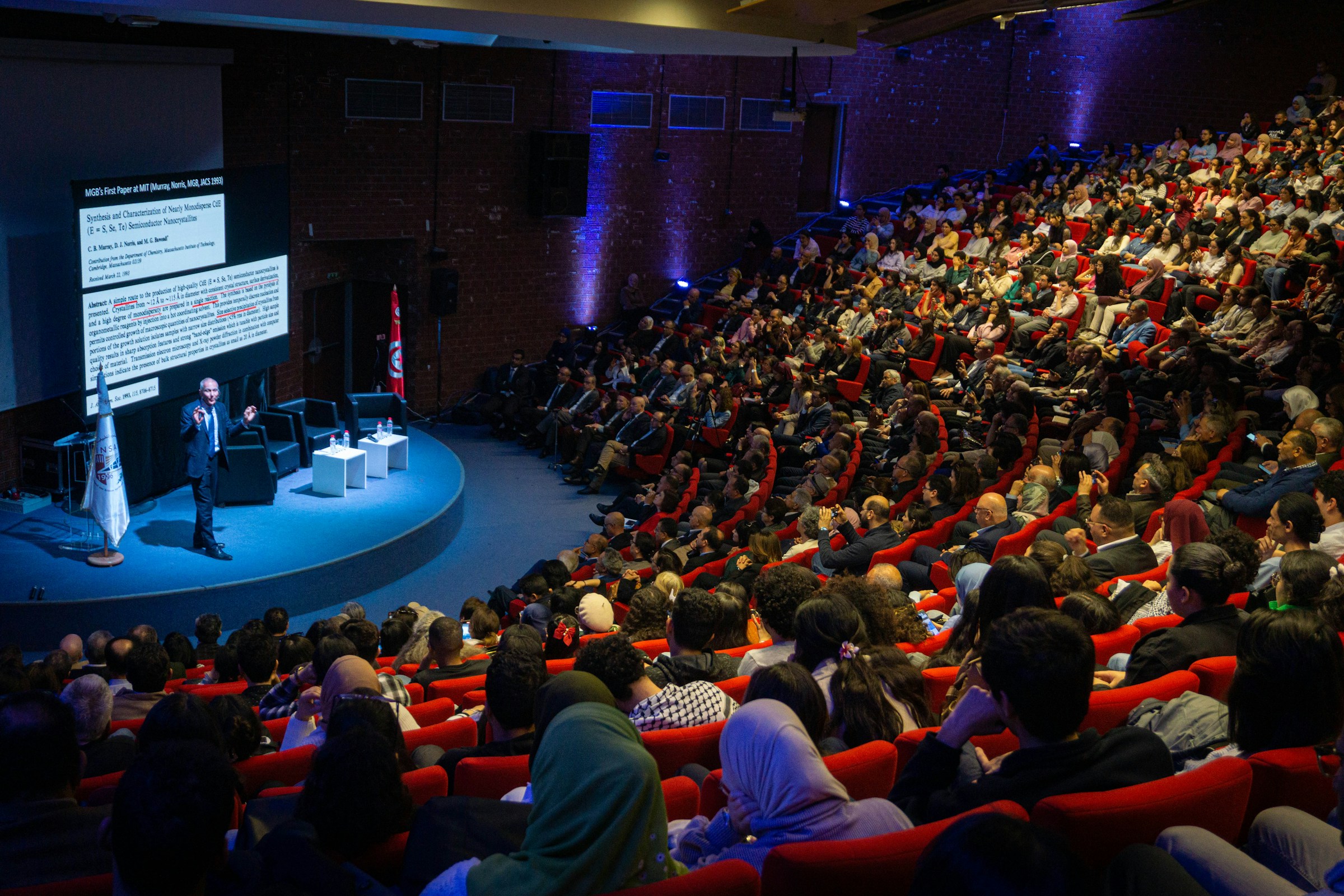 Speaker presenting to a large audience in a conference auditorium